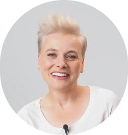 Kobieta z krótkimi, jasnymi włosami, ubrana w jasną bluzkę, która ma przypięty mikrofon do kołnierza, na jasnym tle. Zdjęcie w okrągłej ramce.